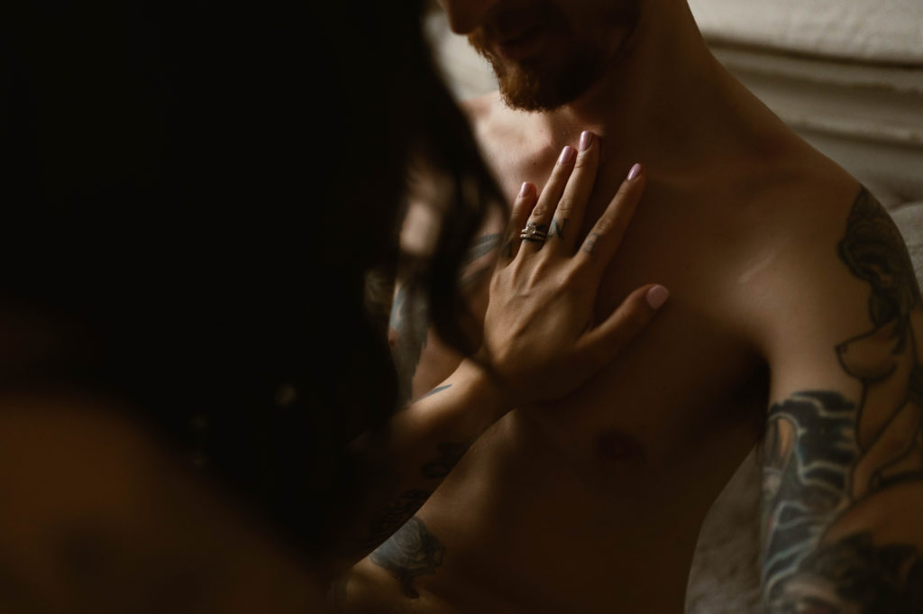 detail photo of a woman's hand with a ring against a man's shirtless chest. 