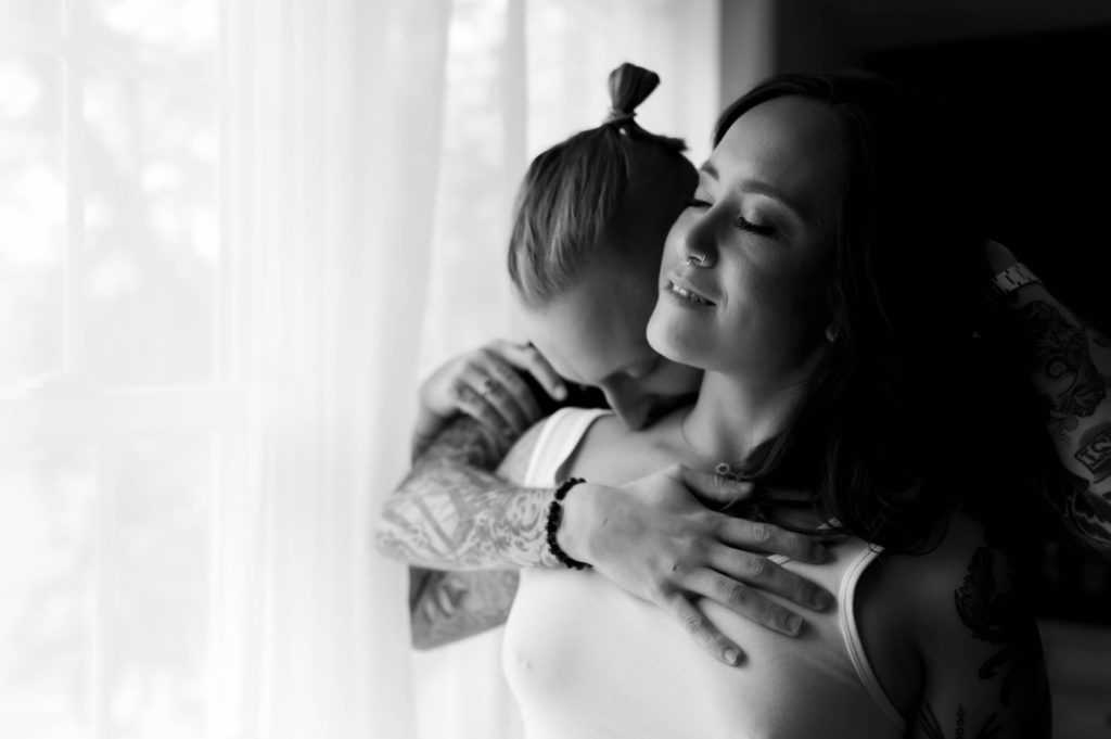 black and white image from couple boudoir session of two people embracing in front of a window.