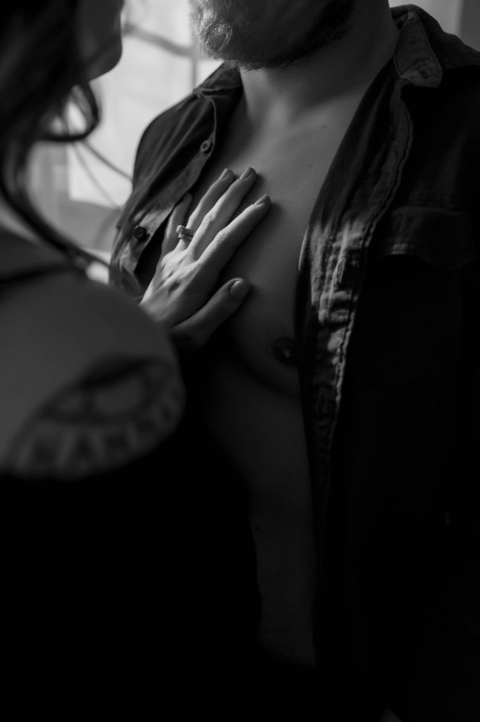 Sultry black and white image of woman's hand with a ring on a man's chest for their session with Virginia Boudoir Photographer