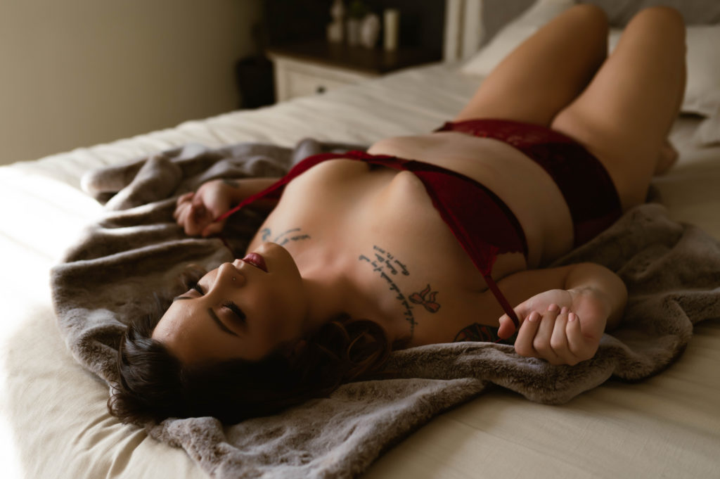 Woman in red lingerie lying across the bed, eyes closed for her session with Virginia Boudoir Photographer