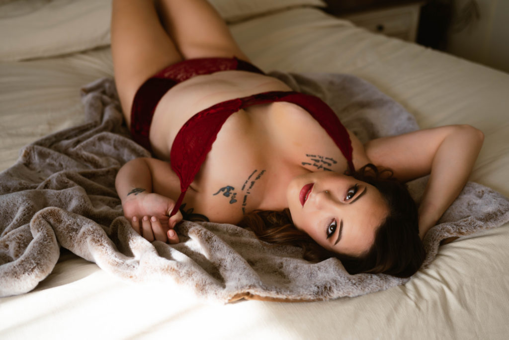 Woman in red lingerie lying on the bed looking back at the camera for her session with Virginia Boudoir Photographer