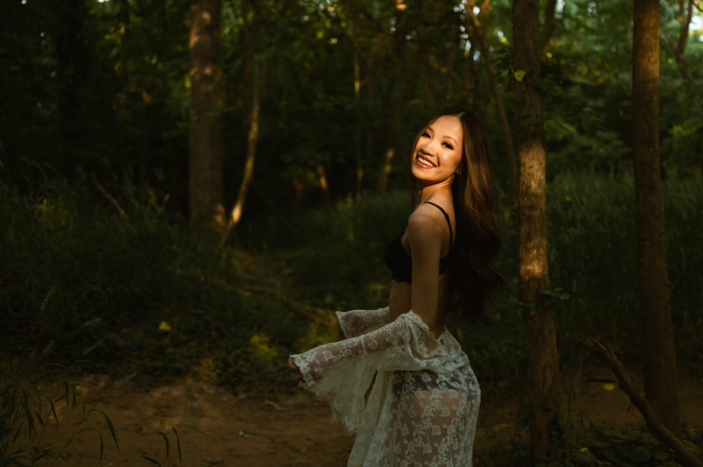 woman in black lingerie and white sheer robe in a forest for her outdoor boudoir shoot.