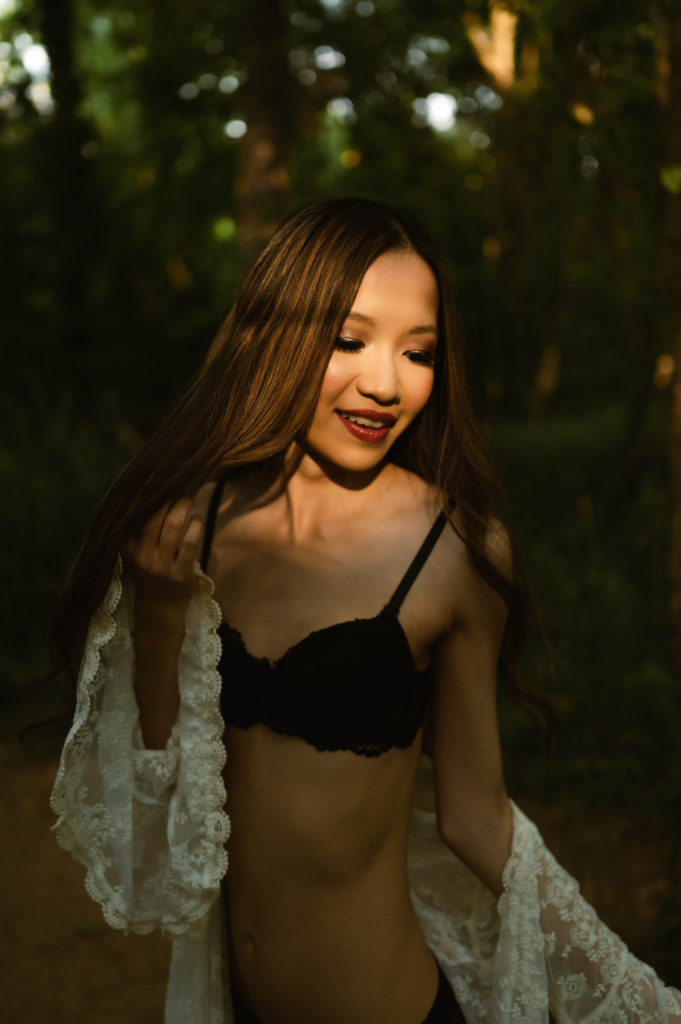 woman in black lingerie and white sheer robe in a forest for her outdoor boudoir shoot.