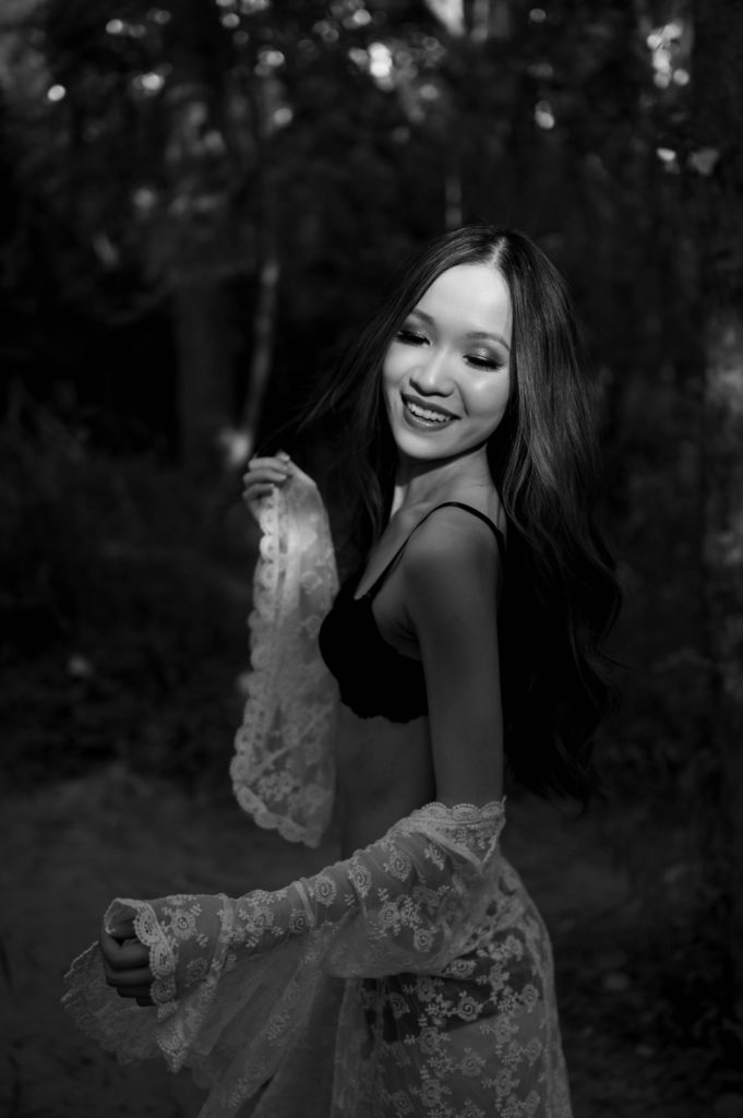 Black and white image of a woman in black lingerie and white sheer robe in a forest for her outdoor boudoir shoot.