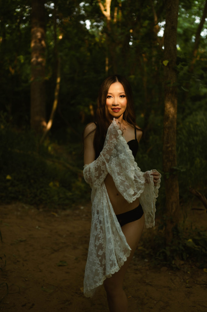 woman in black lingerie and white sheer robe in a forest for her outdoor boudoir shoot.