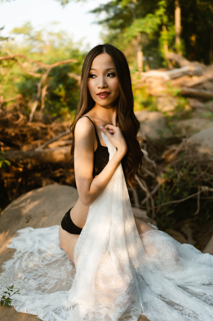 Woman in black lingerie with sheer white robe, sitting next to the water.