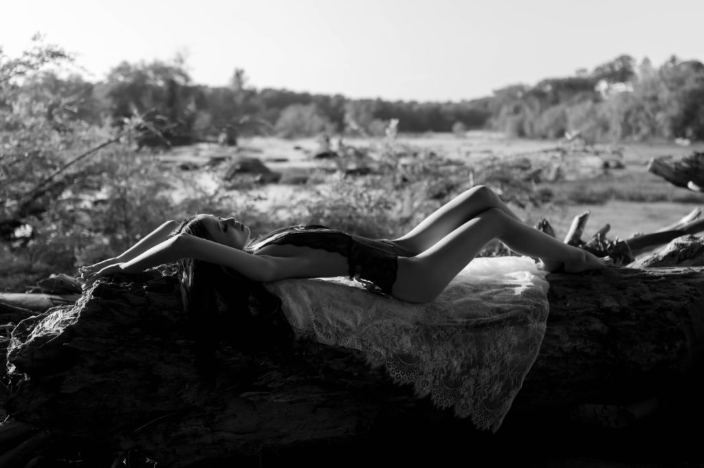 Woman in lacy lingerie lying across a fallen branch for her outdoor boudoir session. 