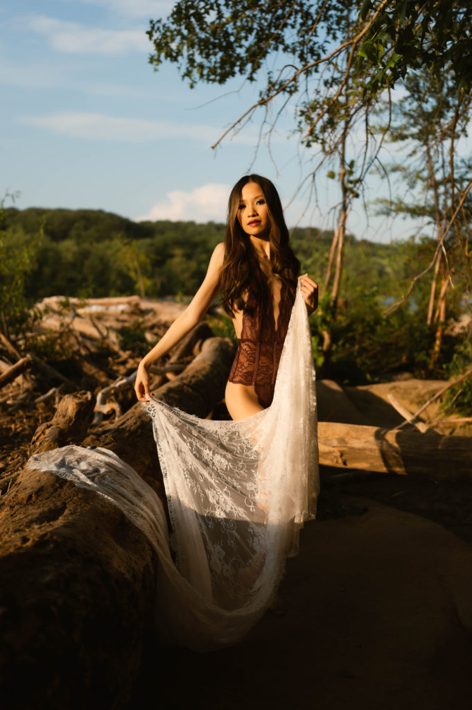 Woman in lace lingerie, holding a sheer white robe at her outdoor boudoir session with Virginia Boudoir Photographer.