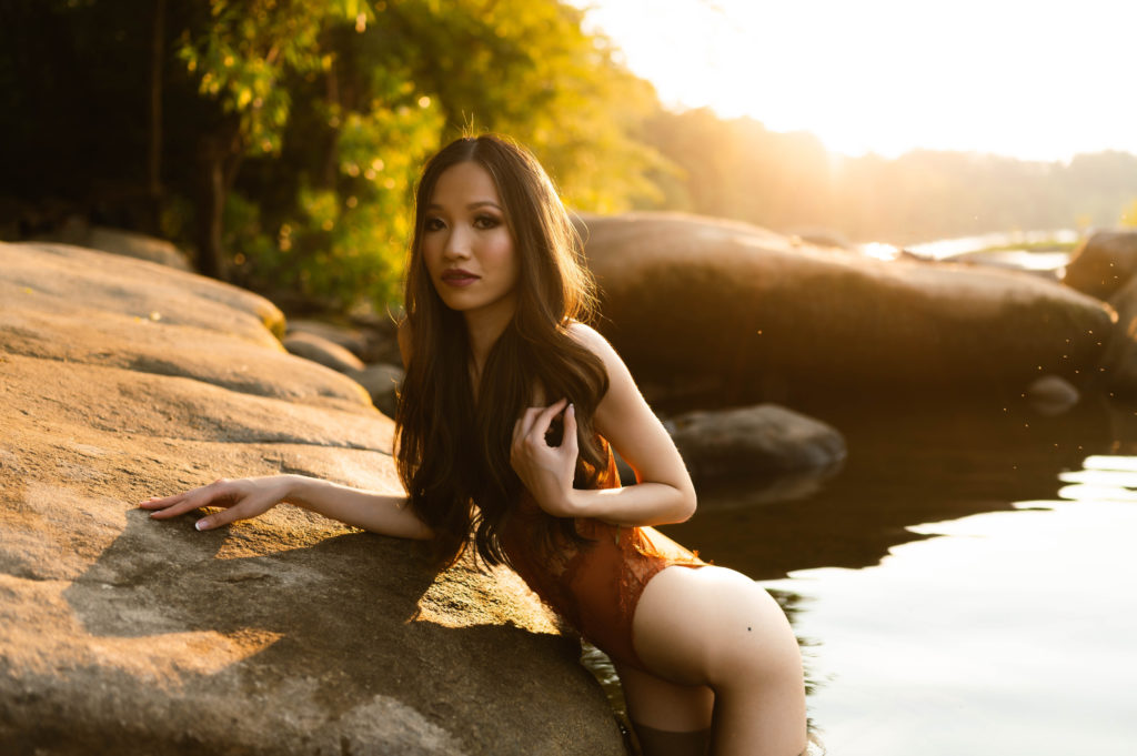 Woman in lace lingerie standing in the water, leaning against a rock.