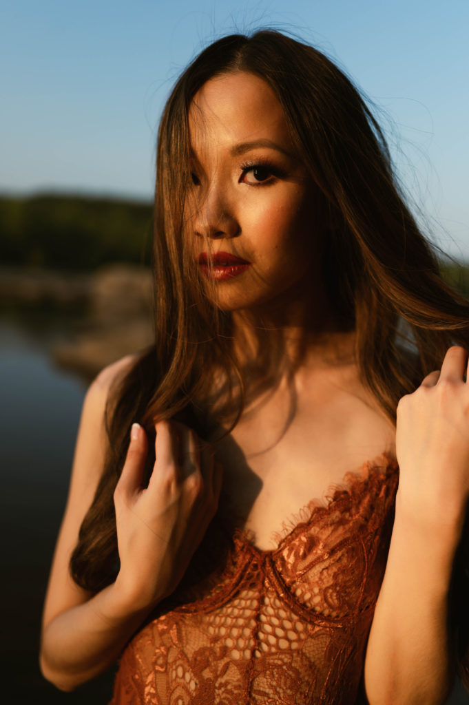 Woman with brunette hair wearing  lingerie and staring into the camera with her hair in front of her face.