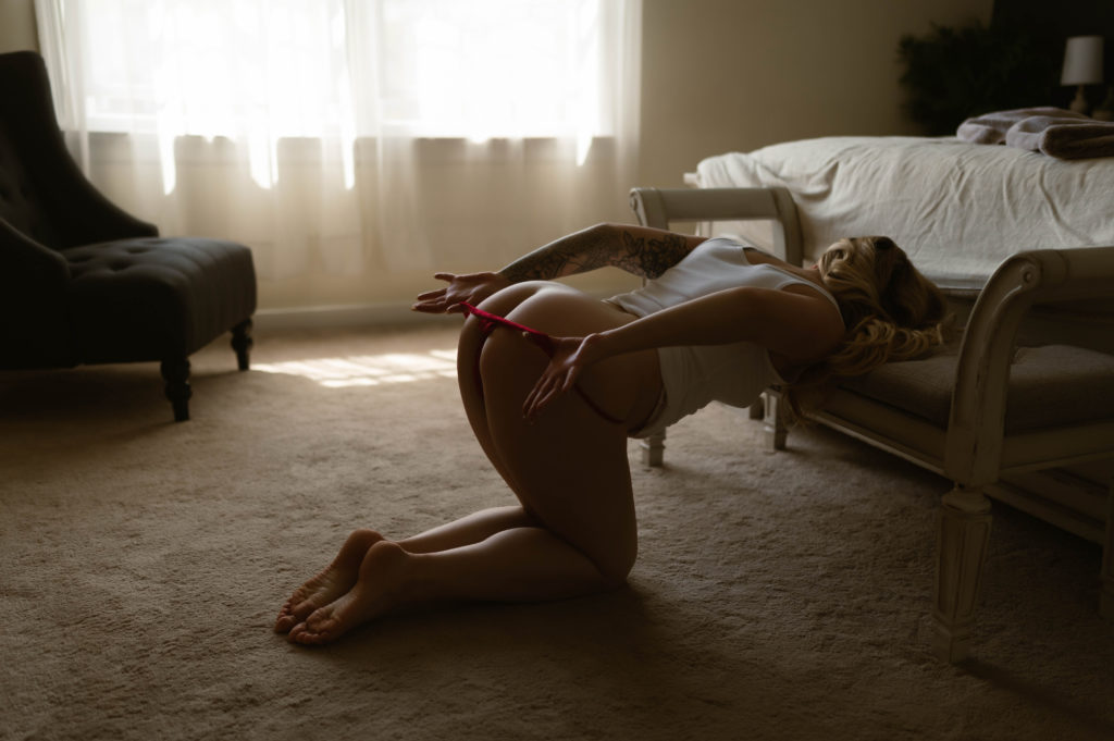 Sexy goddess boudoir shot of a woman taking off her red thong while leaning over a bench.