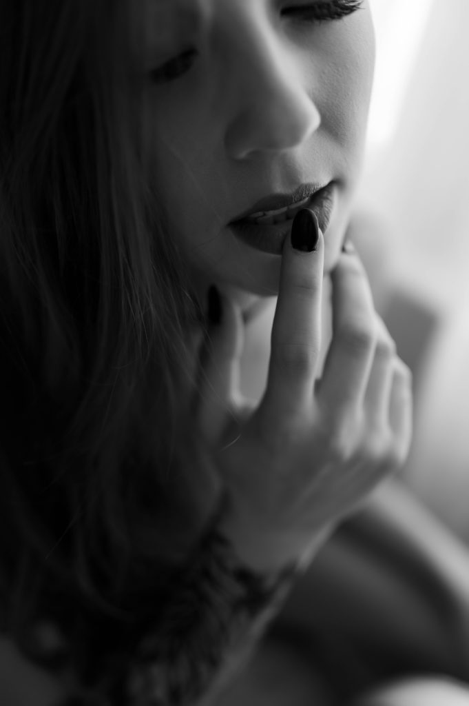 Black and white detail picture of a woman's painted nail against her lip. 