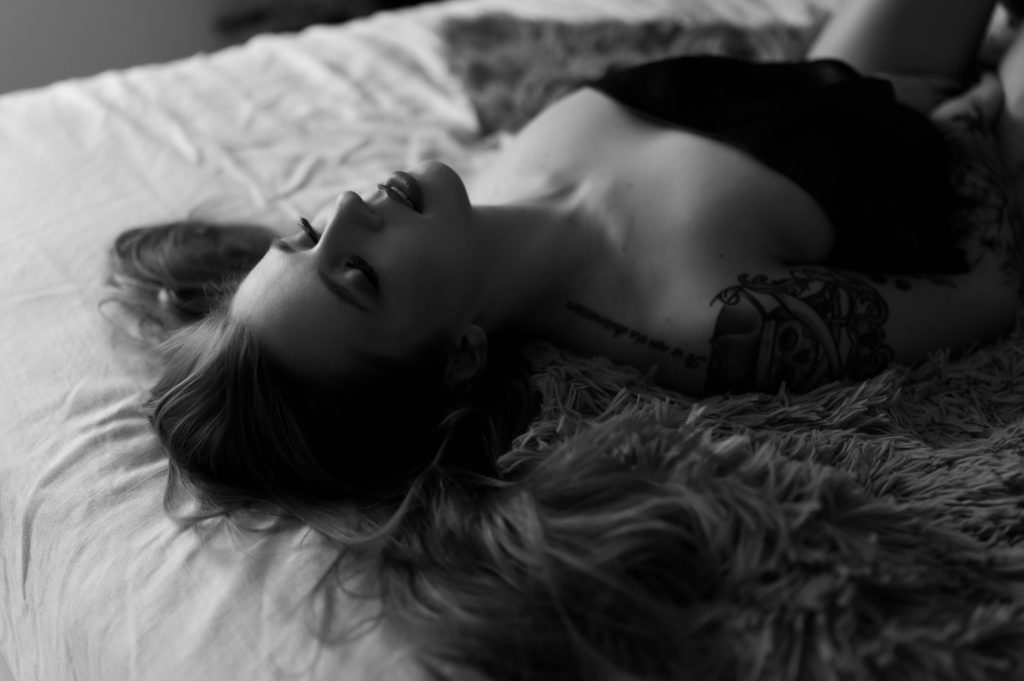 Black and white image of a nude woman lying across a bed covered by a sheet.