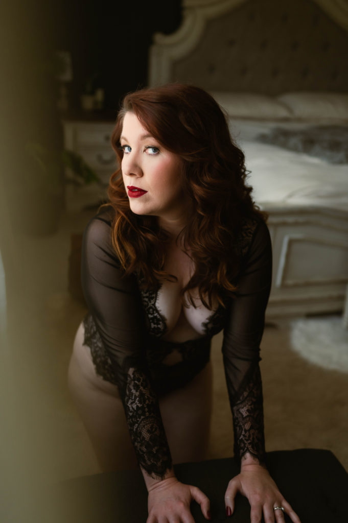 Redhead woman in black sheer lingerie bodysuit, leaning in to the camera.