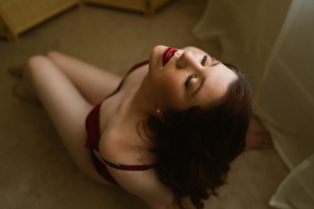 Woman at her boudoir shoot kneeling on the floor with her face up and eyes closed. 