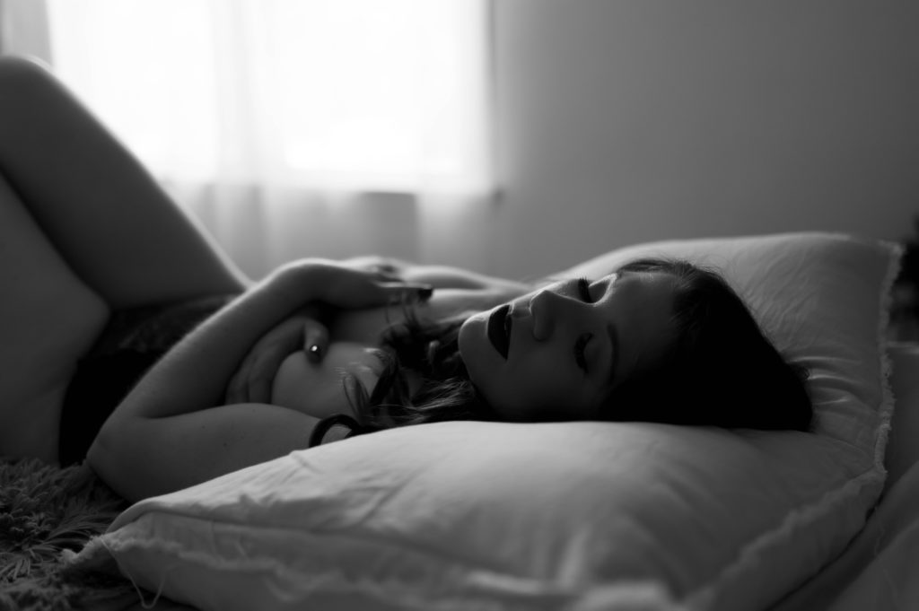 Black and white image of a nude woman lying on a bed for her boudoir session.