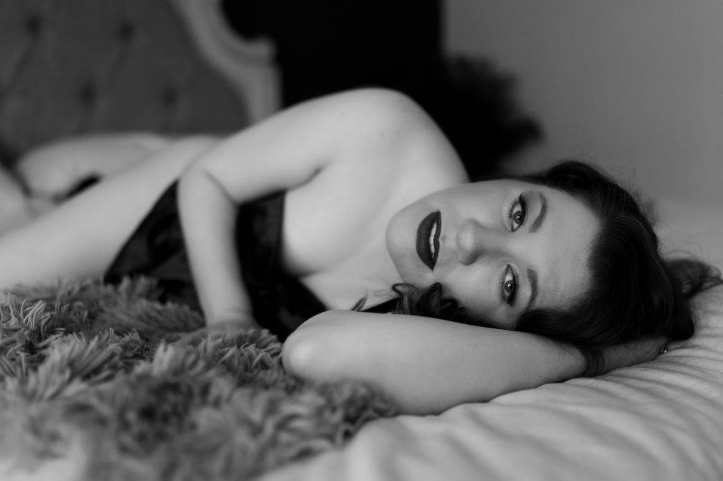 Black and white boudoir photo of a woman wrapped in a sheet looking up at the camera.