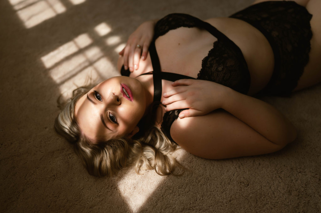 woman in black lingerie lying on the floor under shadows from the window above her.