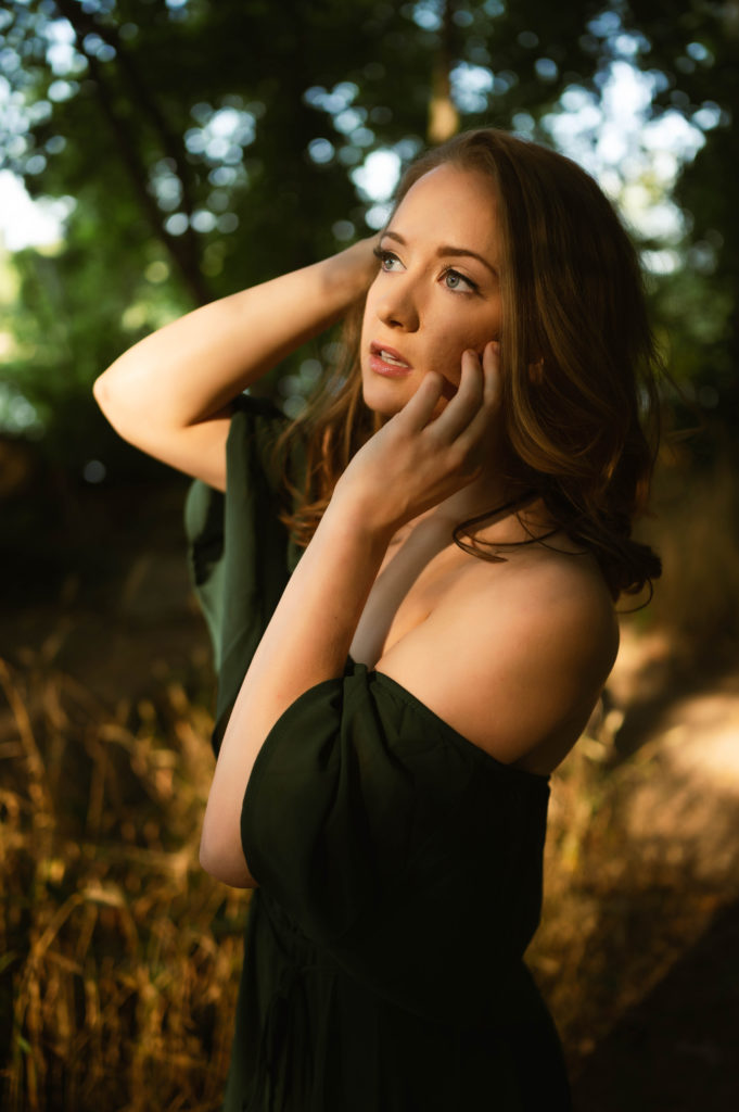 brunette woman outside in the golden sunset with her hands on her face.