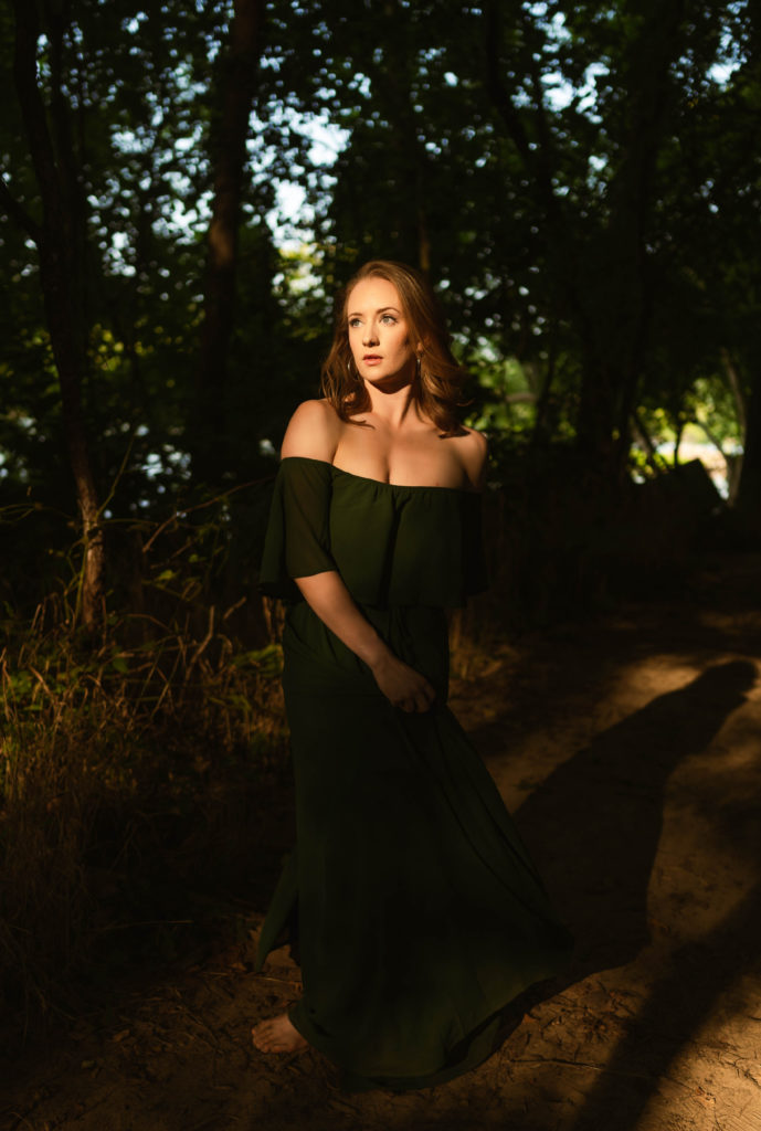 Woman in green off the shoulder dress with the sun shining on her as she spins her dress. 