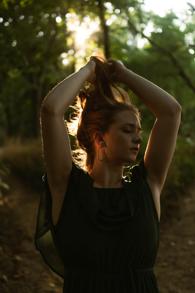 Woman in green off the shoulder dress with her hands running through her hair, looking down. 