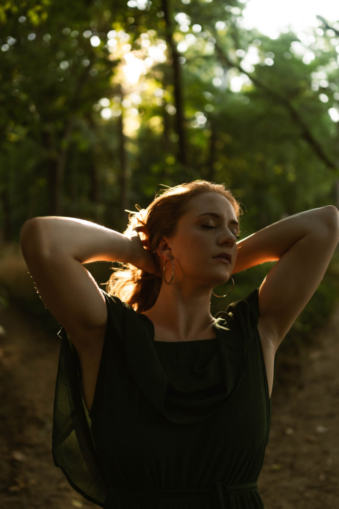 Woman in green off the shoulder dress with her hands in her hair and her eyes closed at her outdoor boudoir session.