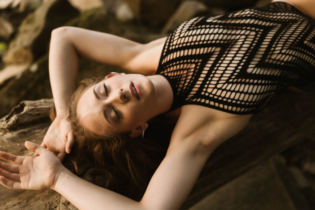 Woman in black lingerie bodysuit, with her hands above her head. 