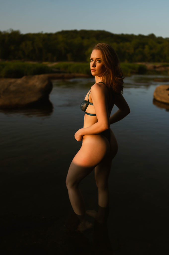 Woman in lace lingerie standing in water, looking back at the camera, in the evening sunlight. 