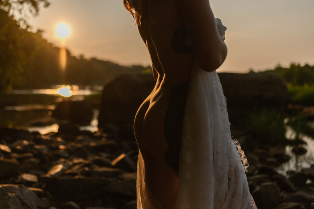 Detail booty shot of a woman covering herself with a lace sheet in the sunset by a lake. 