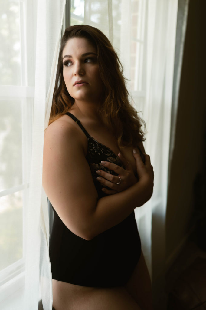 Woman in black lingerie leaning against a window and looking over her shoulder. 