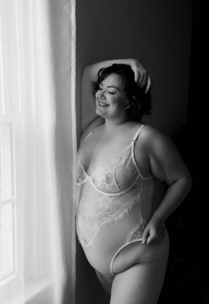 Woman in white lingerie bodysuit standing next to a window. 