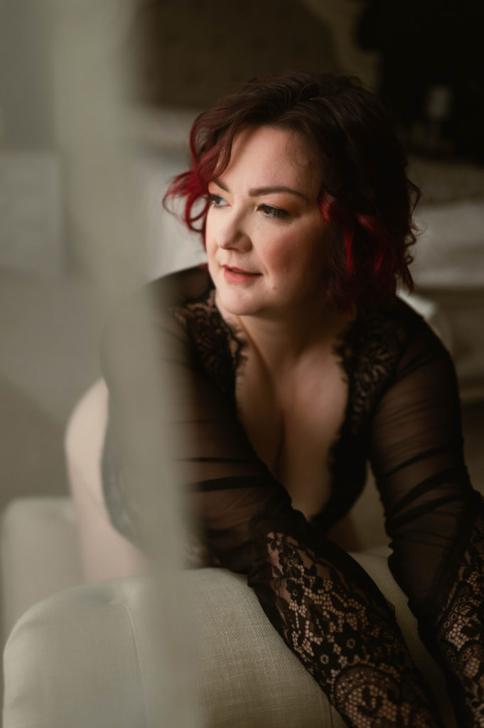 Woman in black lace lingerie leaning over the side of a chair in her boudoir session to help with her body image issues. 