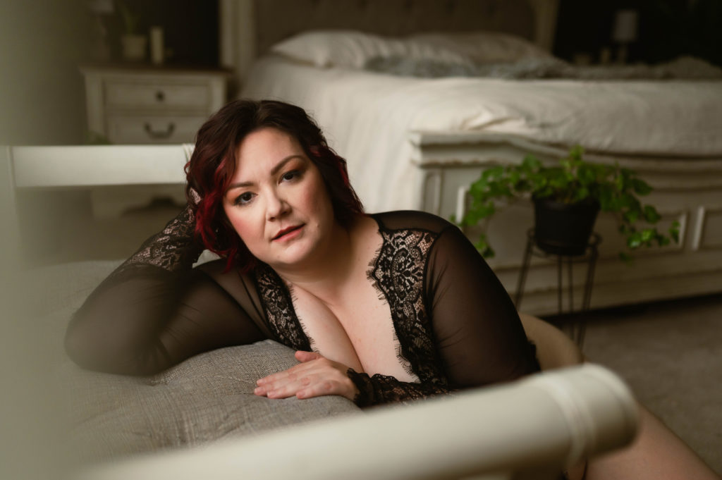 Woman in black lace lingerie leaning over a bench at a boudoir studio. 