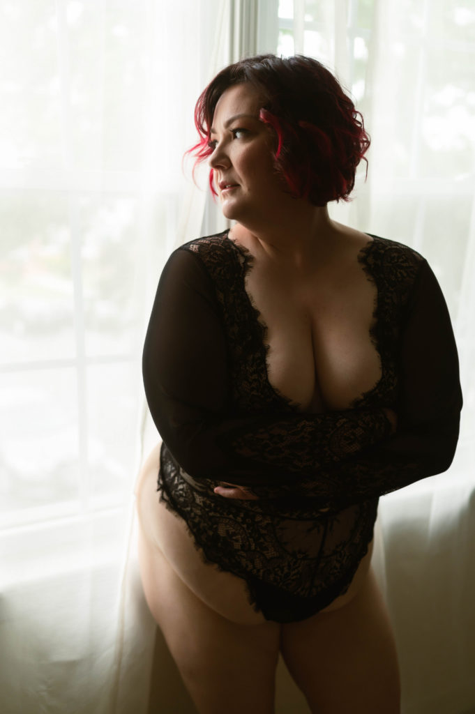 Woman standing next to a window in black lace lingerie. 