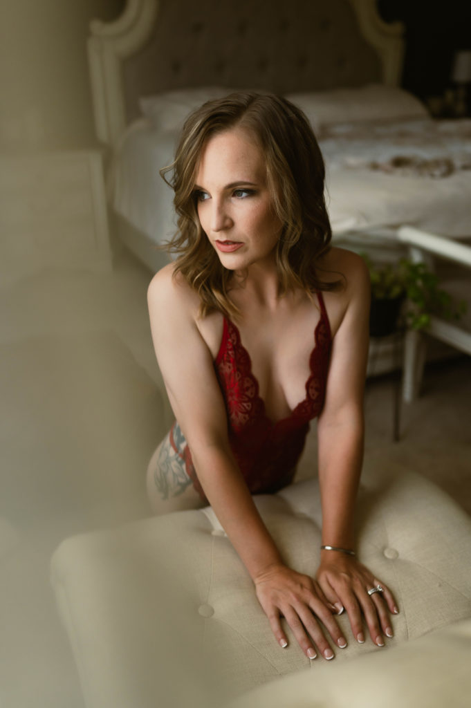 Woman leaning over a chair in red lingerie looking out a window. 