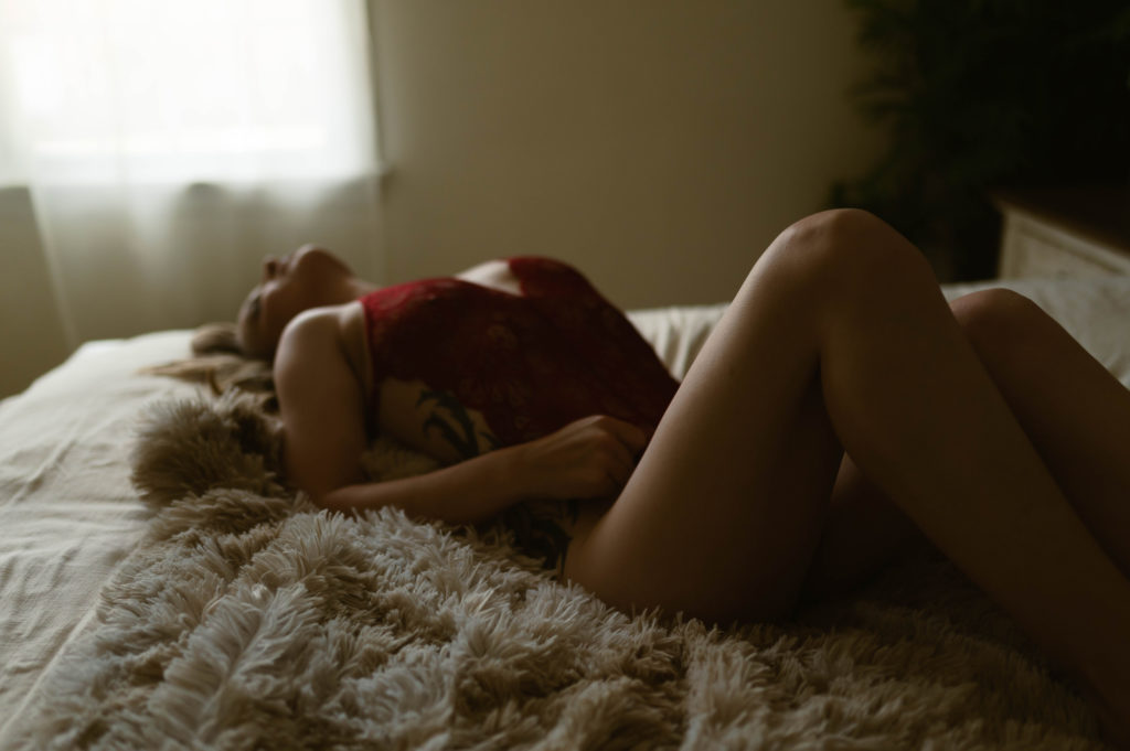 Woman in red lingerie lying across a bed on her back. 