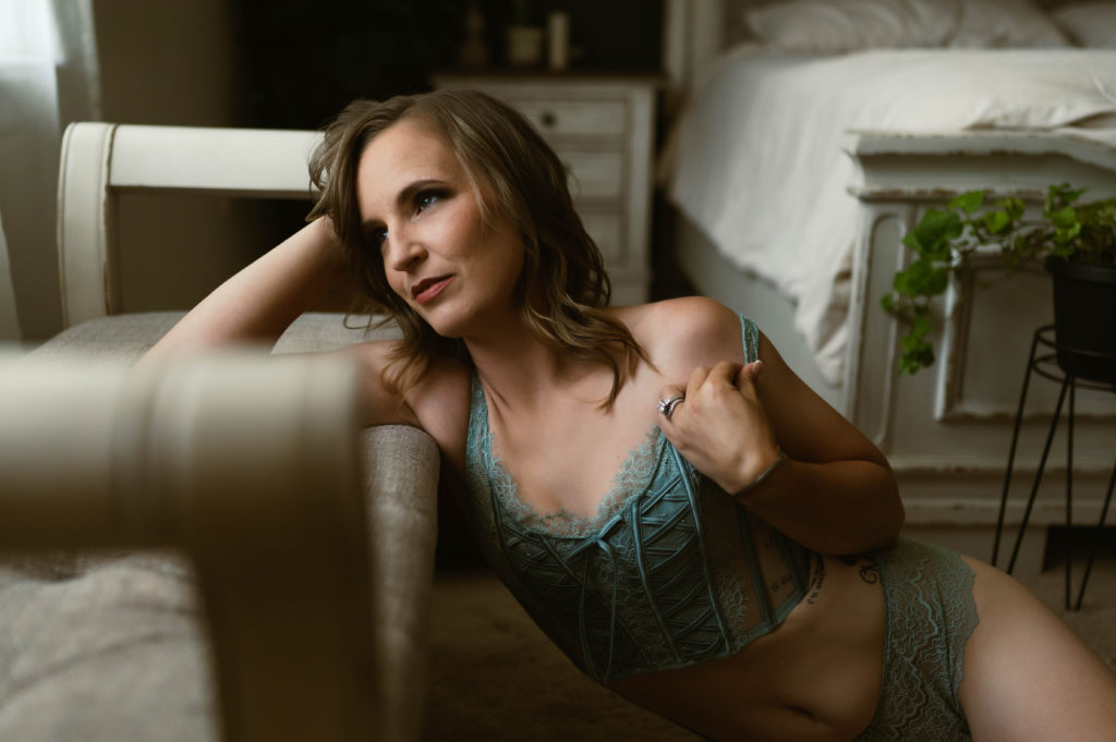 Woman in lingerie corset leaning over a bench, looking out a window. 