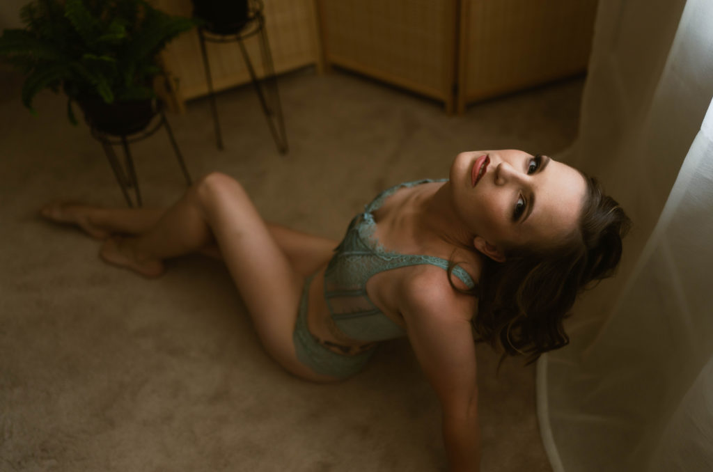 Woman in lingerie sitting on the floor looking up at the camera above. 