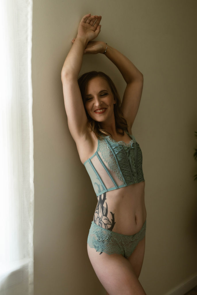 Woman in teal lingerie leaning against a wall for her boudoir session. 