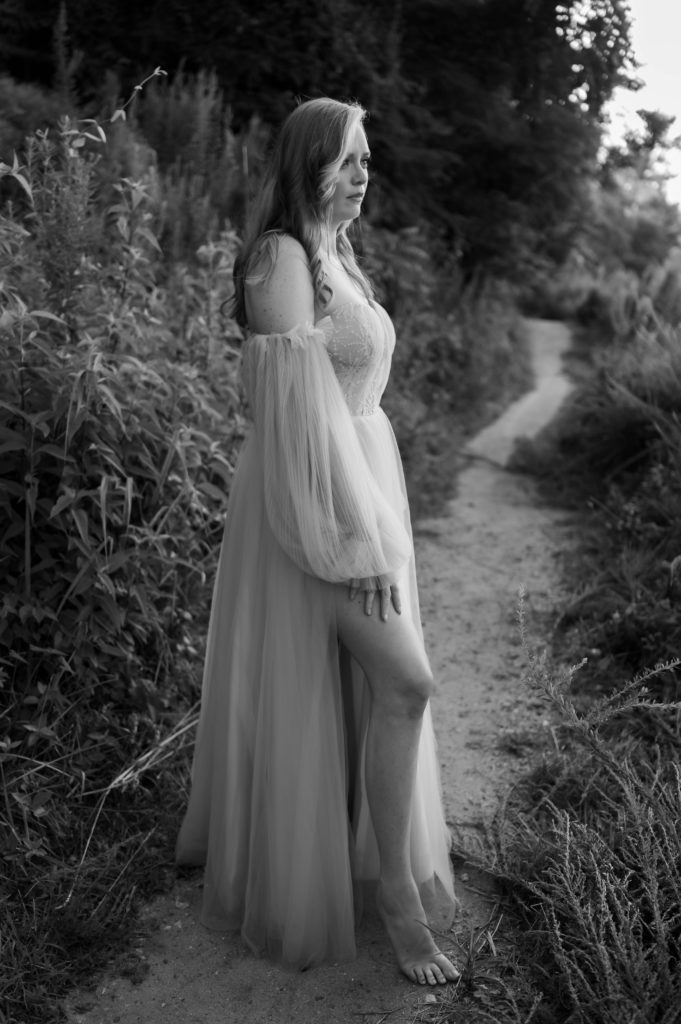 Black and white image of a woman in off the shoulder fancy dress outside on a path. 