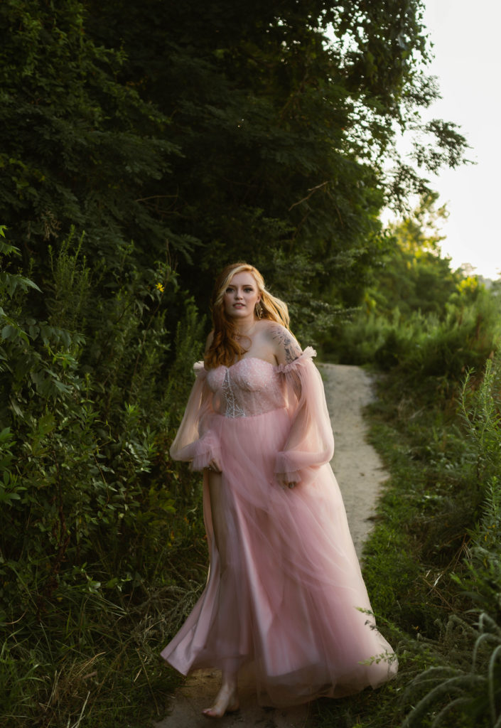 Woman in a pale pink tulle dress running down a path outside.