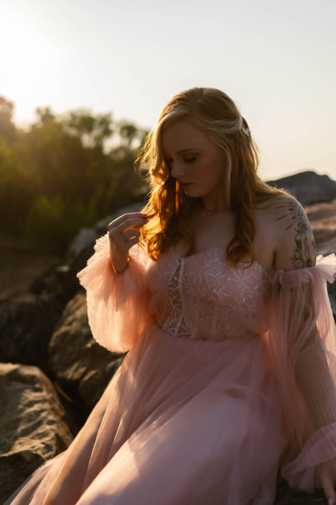 Woman in pale pink tulle dress sitting outside in the sunset light. 