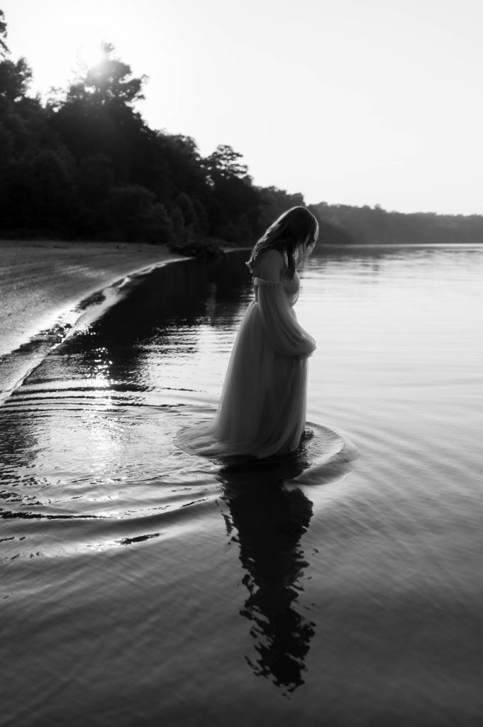 Black and white photo of a woman walking in the water in a tulle dress.