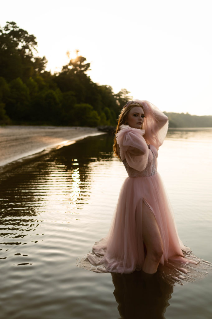 Woman in pink tulle dress posing while standing in the water for her boudoir session. 