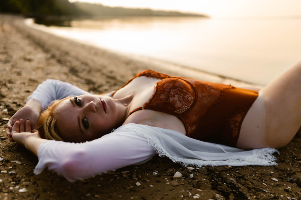 Woman in red lingerie lies on the beach for her in the water boudoir session. 