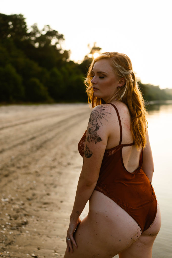 Woman in red lingerie kneeling on the shore of water looking over her shoulder in the golden light.