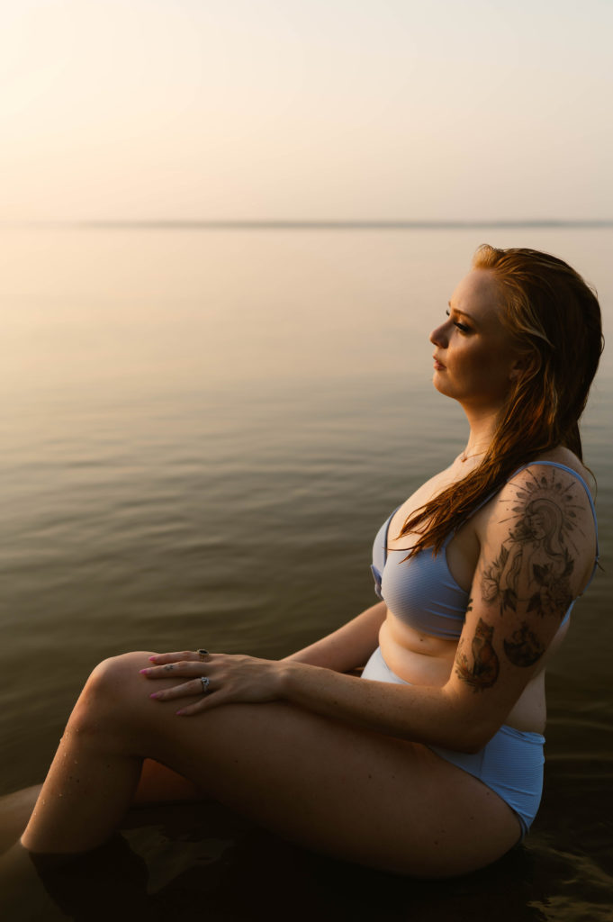 Woman in blue swim suit sitting next to the lake. 