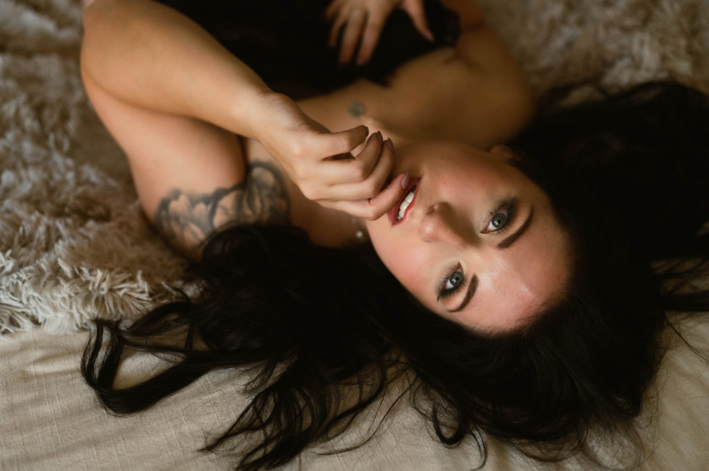 Nude woman covering herself with a sheet while lying on a bed.