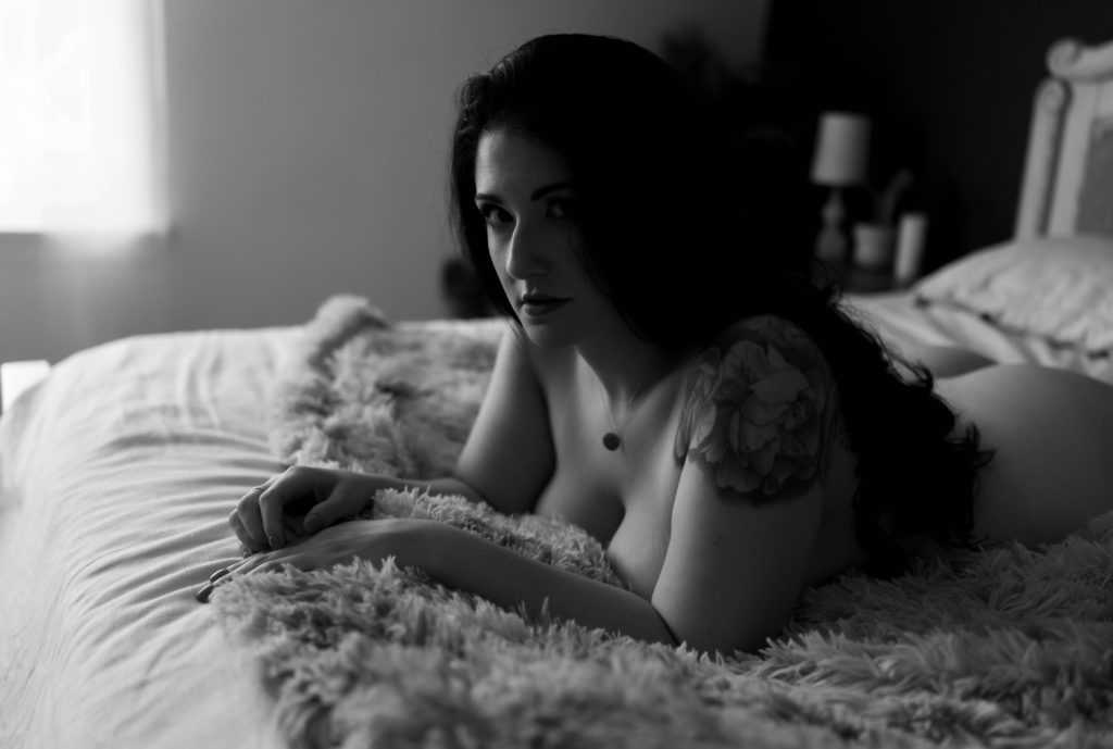 Black and white image of a nude woman lying across a bed.