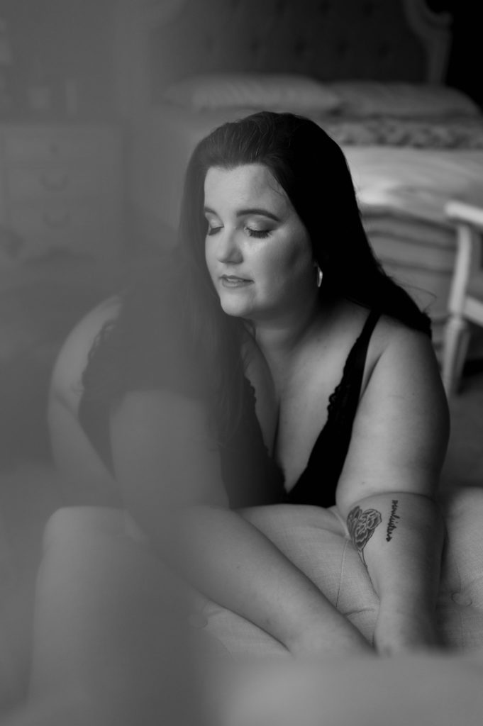 Black and white image of a woman kneeling over a bench in lingerie for her boudoir session. 